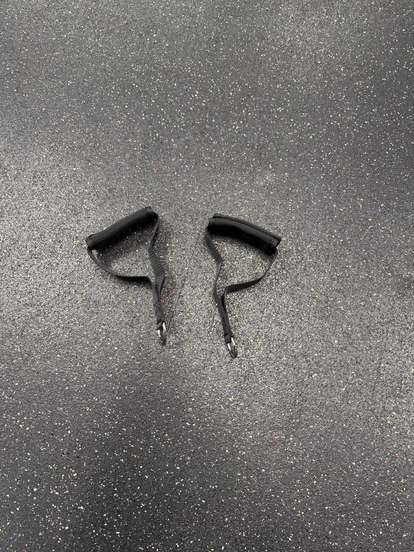 Pair of black cable machine handles with carabiner clips placed on a rubber gym floor.