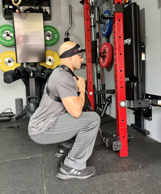 Man demonstrating proper form in a squat harness review at the gym with equipment in the background.