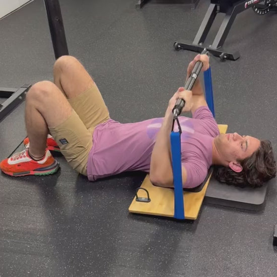 Man performing a resistance band bench press variation while lying on a wooden platform in a gym.