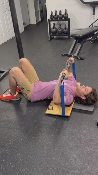 Man performing a resistance band bench press variation while lying on a wooden platform in a gym.